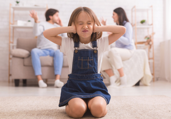 Kind kniet auf dem Boden und hält sich die Ohren zu, während Eltern sich streiten