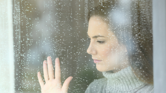Frau mit leerem Blick hinter verregnetem Fenster - Anzeichen und Symptome Depression