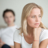 Verzweifelte Frau, im Hintergrund sitzt Ihr Mann - eine Affäre, tiefer Einschnitt in der Beziehung