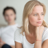 Eine Frau ist nachdenklich und verzweifelt, im Hintergrund sitzt Ihr Mann - Paartherapie bei Aufarbeitung einer Affäre