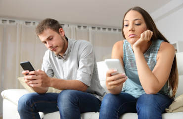 Paar sitzt nebeneinander, jeder schaut gelangweilt in sein Handy - Langeweile in der Beziehung