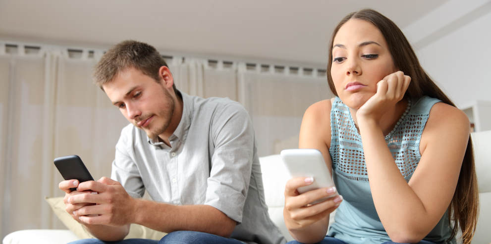 Eine Frau und ein Mann sitzen nebeneinander und schauen gelangweilt in Ihr Handy