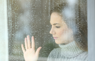 Frau mit leerem Blick hinter verregnetem Fenster - Angehörige leiden mit