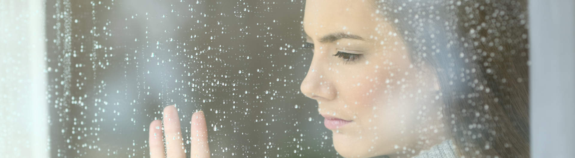 Frau mit leerem Blick hinter verregnetem Fenster - Behandlung von Depressionen